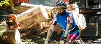 Biker fährt durch Gebiet, wo forstliche Arbeiten durchgeführt werden © Land Tirol Mountainbikefahrer fährt mit erschrockenen Gesicht auf ein Stahlseil zu, welches auf Kopfhöhe gespannt ist. Im Hintergrund sind forstarbeiten am Gange